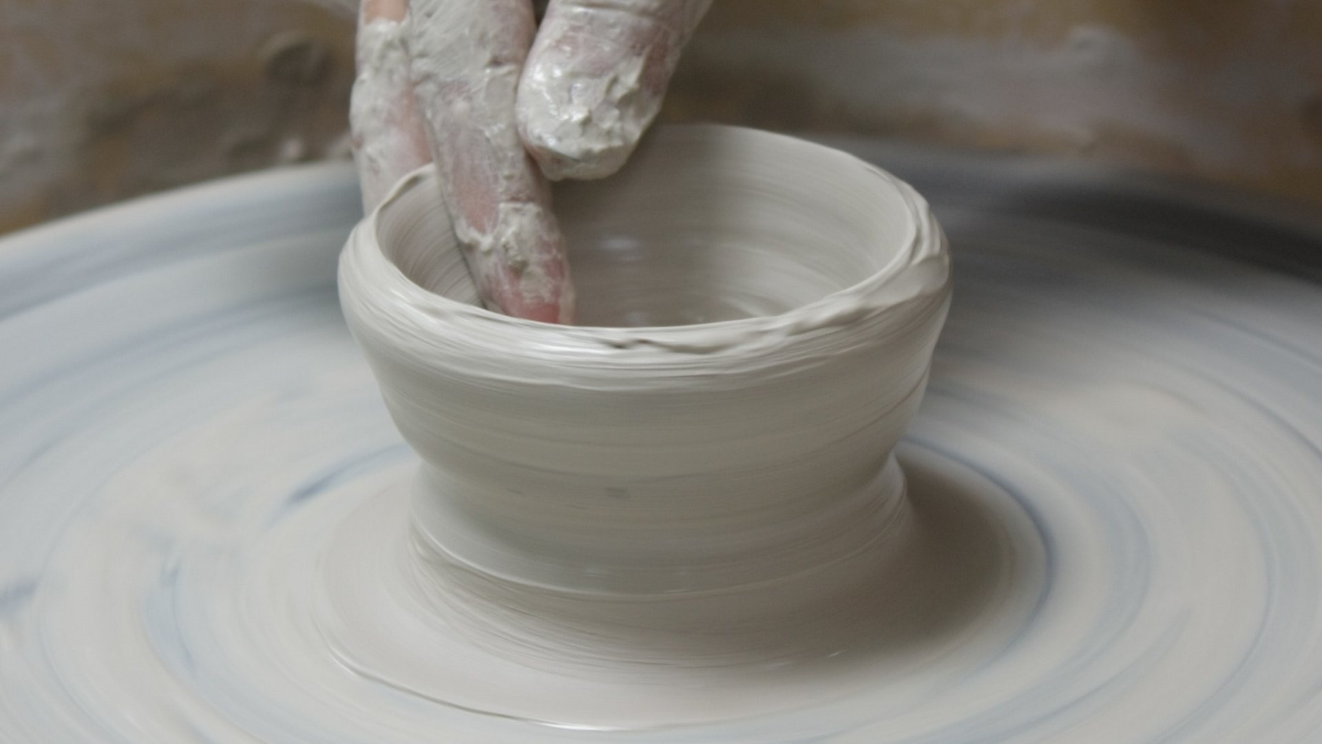 a potter makes a clay bowl on a wheel